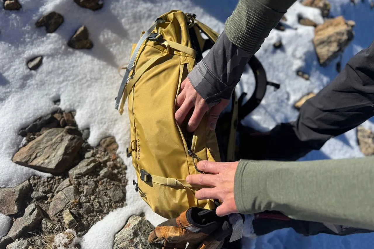 在雪地上打开 Gregory Alpinisto 30 背包的侧拉链口袋